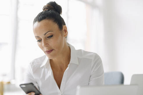 Selbstbewusste Unternehmerin, die im Büro zu Hause sitzt und ein Smartphone benutzt - JOSEF01277