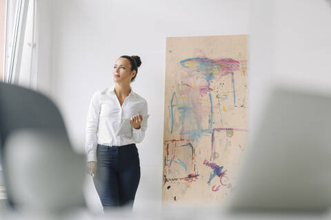 Thoughtful businesswoman holding digital tablet while standing against wall in home office stock photo