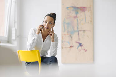 Businesswoman talking over smart phone while sitting on chair in home office - JOSEF01288