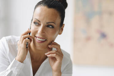 Close-up of smiling businesswoman talking over mobile phone looking away in home office - JOSEF01292