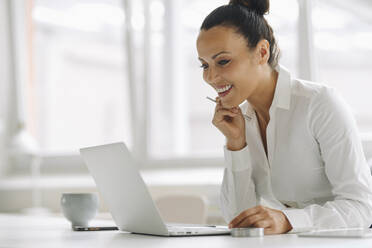 Smiling businesswoman using laptop on desk in home office - JOSEF01299