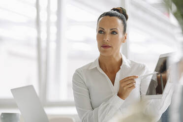 Close-up of confident businesswoman holding digital tablet while sitting in home office - JOSEF01303