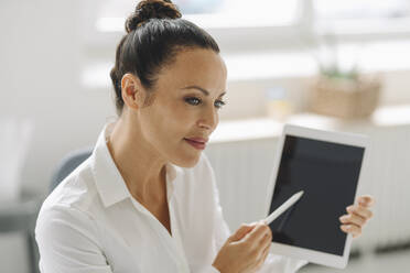 Close-up of female entrepreneur holding digital tablet looking away in home office - JOSEF01305