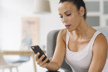 Nahaufnahme einer Geschäftsfrau, die ein Smartphone benutzt, während sie zu Hause sitzt - JOSEF01322