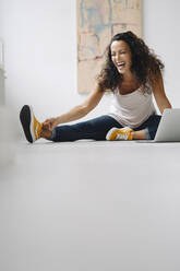 Frau lacht, während sie zu Hause mit ihrem Laptop auf dem Boden sitzt - JOSEF01330