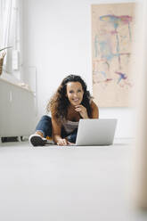 Smiling mid adult woman using laptop on floor at home - JOSEF01331