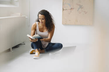 Mid adult woman reading book while sitting on floor at home - JOSEF01345