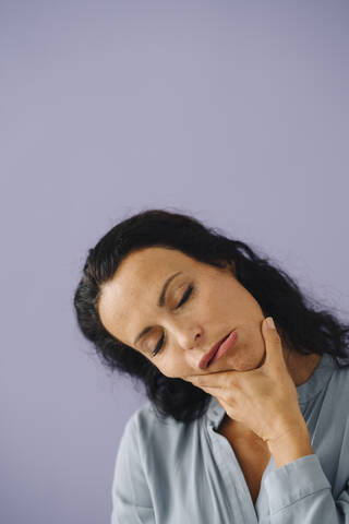 Close-up of woman with eyes closed making face against purple background stock photo