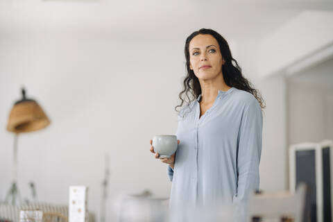 Thoughtful female owner holding coffee mug while standing in cafe stock photo