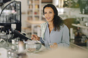 Smiling female barista looking away while working at counter in cafe - JOSEF01395