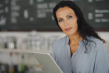 Confident female barista holding digital tablet while working in cafe - JOSEF01401