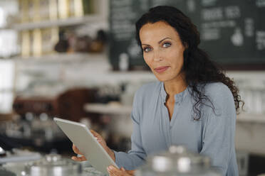 Confident female owner using digital tablet while standing in restaurant - JOSEF01406