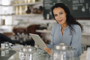 Selbstbewusste Besitzerin, die ein digitales Tablet benutzt, während sie am Tresen eines Restaurants steht - JOSEF01407