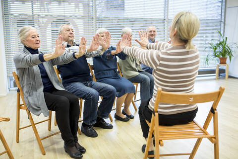 Group of seniors practicing chair gymnastics with instructor in retirement home stock photo
