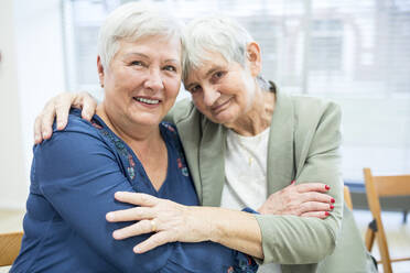 Two senior women embracing in retirement home - WESTF24597