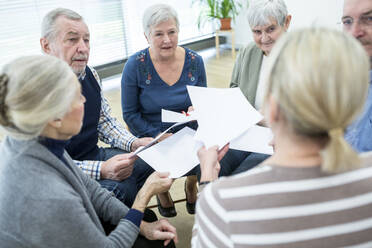 Gruppe von Senioren, die an einer Therapiegruppe in einem Altenheim teilnehmen, mit Papierblättern - WESTF24608