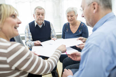 Gruppe von Senioren, die an einer Therapiegruppe in einem Altenheim teilnehmen, mit Papierblättern - WESTF24609