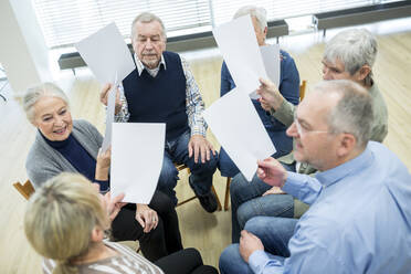 Gruppe von Senioren, die an einer Therapiegruppe in einem Altenheim teilnehmen, mit Papierblättern - WESTF24611