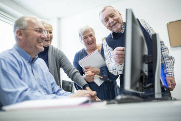 Aktive Senioren, die einen Computerkurs besuchen, den Kursleiter beobachten und sich Notizen machen - WESTF24645