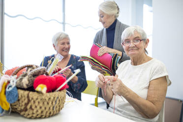Senior women knitting toghether in needlework group of retirement home - WESTF24691