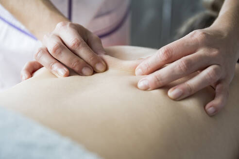 Die Hände einer Physiotherapeutin massieren den Rücken einer Frau - ABZF03255