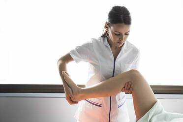 Physiotherapeutin behandelt das Bein einer Patientin - ABZF03268
