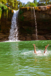 Beine einer anonymen Person, die in der Nähe eines beeindruckenden Wasserfalls an einem sonnigen Tag in Spanien plantscht - ADSF00454