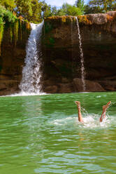 Legs of anonymous person splashing near amazing waterfall on sunny day in Spain - ADSF00454
