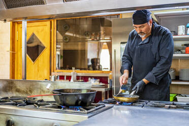 Chef with pan in traditional Spanish restaurant kitchen - DLTSF00844