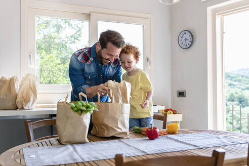Lächelnder Mann zeigt seinem Sohn in der Küche zu Hause Lebensmittel - EIF00014