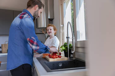 Cute boy looking at father washing cherry tomatoes in kitchen sink - EIF00026