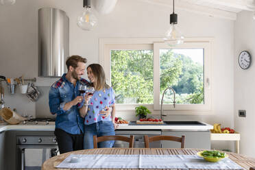 Glückliches Paar in der Mitte des Erwachsenenalters genießt Wein, während es in der Küche zu Hause steht - EIF00029
