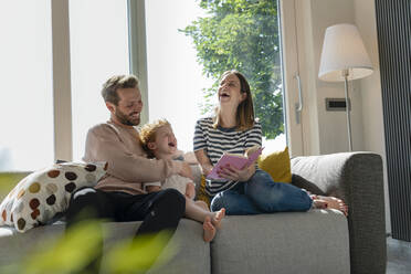 Fröhliche Familie, die zu Hause auf dem Sofa sitzend ein Märchenbuch liest - EIF00041