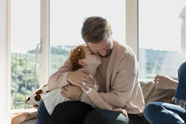 Man embracing cute preschool son while sitting by woman in living room at home - EIF00042