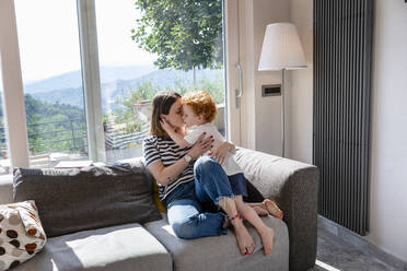 Mutter küsst süßen Sohn, während sie auf dem Sofa im Wohnzimmer zu Hause sitzt - EIF00043