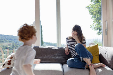 Junge rennt auf die Mutter zu, die zu Hause mit der Hand über den Augen sitzt - EIF00044