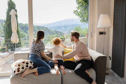 Familie schaut aus dem Fenster, während sie auf dem Sofa im Wohnzimmer sitzt - EIF00047