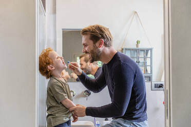 Glücklicher Mann putzt die Zähne seines Sohnes mit einer Zahnbürste im Badezimmer zu Hause - EIF00056