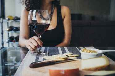 Junge Frau hält ein Weinglas, während sie am Esstisch sitzt - SBAF00014