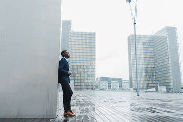 African-American businessman leaning on wall outdoors - ADSF00501