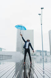Ethnischer Mann, der auf dem Bürgersteig stehend einen Regenschirm auffängt - ADSF00508
