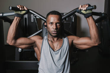 Serious African American guy listening to music and performing exercise on modern machine during workout in gym - ADSF00549