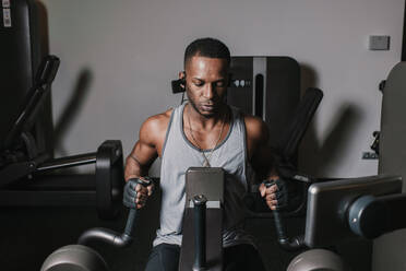 Schwarzer Mann trainiert an einem Gerät im Fitnessstudio - ADSF00550