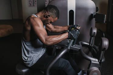 Schwarzer Mann trainiert an einem Gerät im Fitnessstudio - ADSF00552