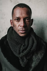 Handsome African American male in stylish warm clothes standing near concrete wall - ADSF00569