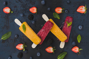 View from above of yellow and red ice creams on dark background with strawberries blackberries blueberries and mint - ADSF00587