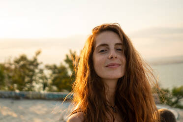 Attraktive junge Frau, die lächelt und in die Kamera schaut, während sie auf einem unscharfen Hintergrund von erstaunlicher Natur an einem sonnigen Tag in Bulgarien, Balkan, steht - ADSF00590