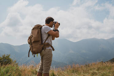 Rückenansicht eines Mannes mit Rucksack, der eine professionelle Kamera benutzt, um Fotos von einer malerischen Landschaft in Bulgarien, Balkan, zu machen - ADSF00593