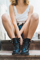 Gesichtslose Aufnahme einer Frau in sommerlich modischen Shorts und brutalen schwarzen Stiefeln, die auf den Stufen im Freien sitzt - ADSF00609