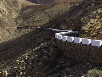 Hübscher weißer Zaun an der Seite einer kurvenreichen Asphaltstraße am Hang eines wunderschönen Hügels auf der Insel Fuerteventura, Spanien - ADSF00633